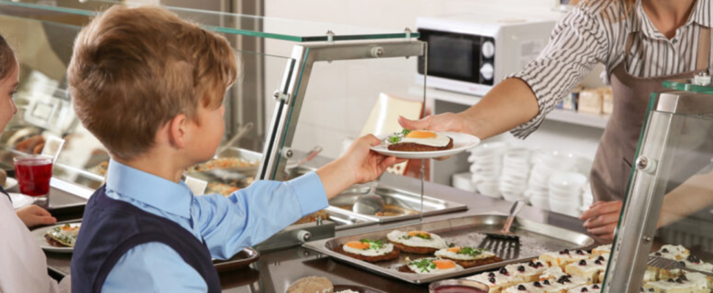 Un enfant se fait servir à manger par une femme dans une cantine.