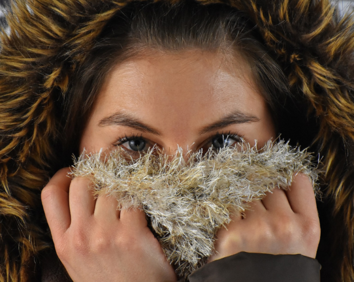 Une femme se couvre le bas du visage avec une écharpe et porte une capuche recouverte de fourrure.